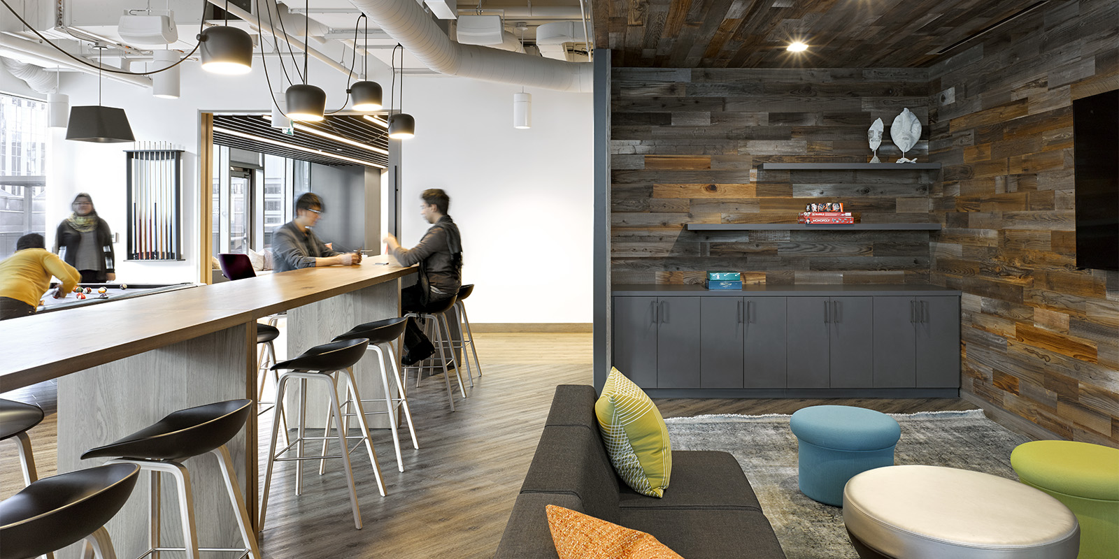 OMERS office social zone with bar seating, industrial lighting, wood wall, and colourful upholstery