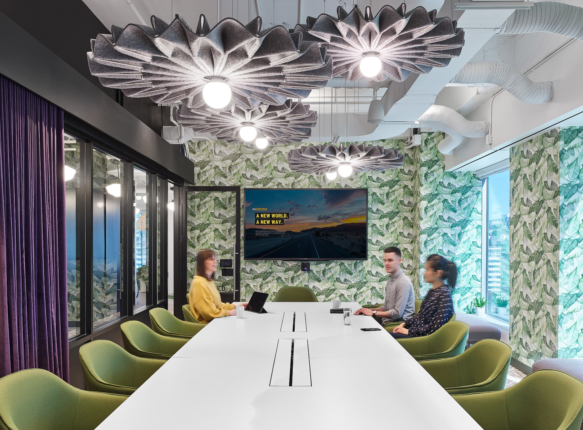 Mediabrands meeting room with green chairs, palm leaf wallpaper, grey folded light fixtures, and purple curtains