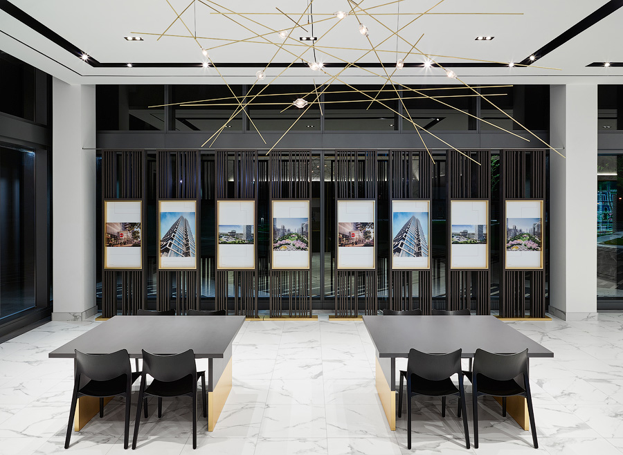 Transit City sales area with tables and chairs, renderings on wall, white marble floors, and modern brass light fixture